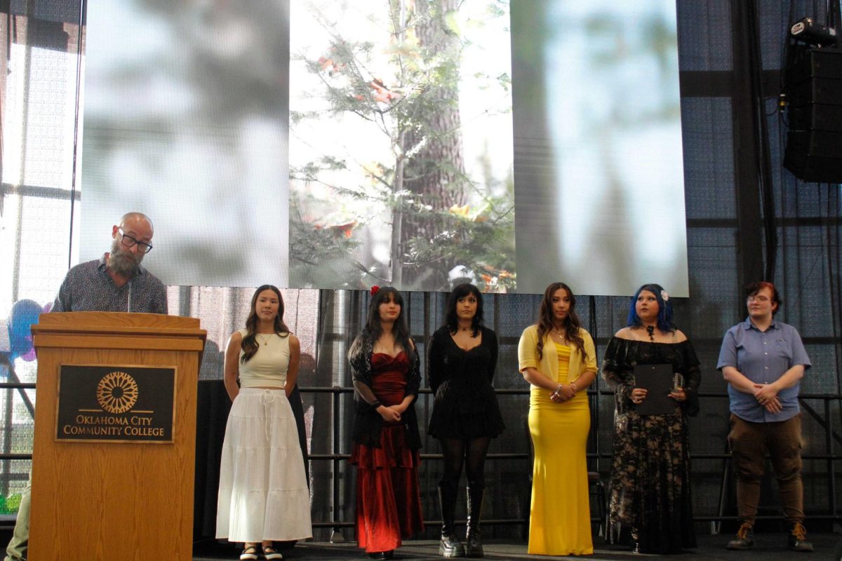 Following a reception held to kick off this year's visual arts capstone exhibition, Chair of Visual Arts Jeremy Fineman (far left) showcases student artwork on the big screen while celebrating the achievements of OCCC students (from left) Maya Cantwell, Angie Vargas, Ashley Allen, Gaby Cabrera, Gabriela Ordunez and Emerson Taylor.